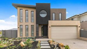 A modern two-story house with a garage, a circular window, and a well-maintained garden.