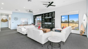 A modern living room with white sofas, a coffee table, and a TV wall unit.