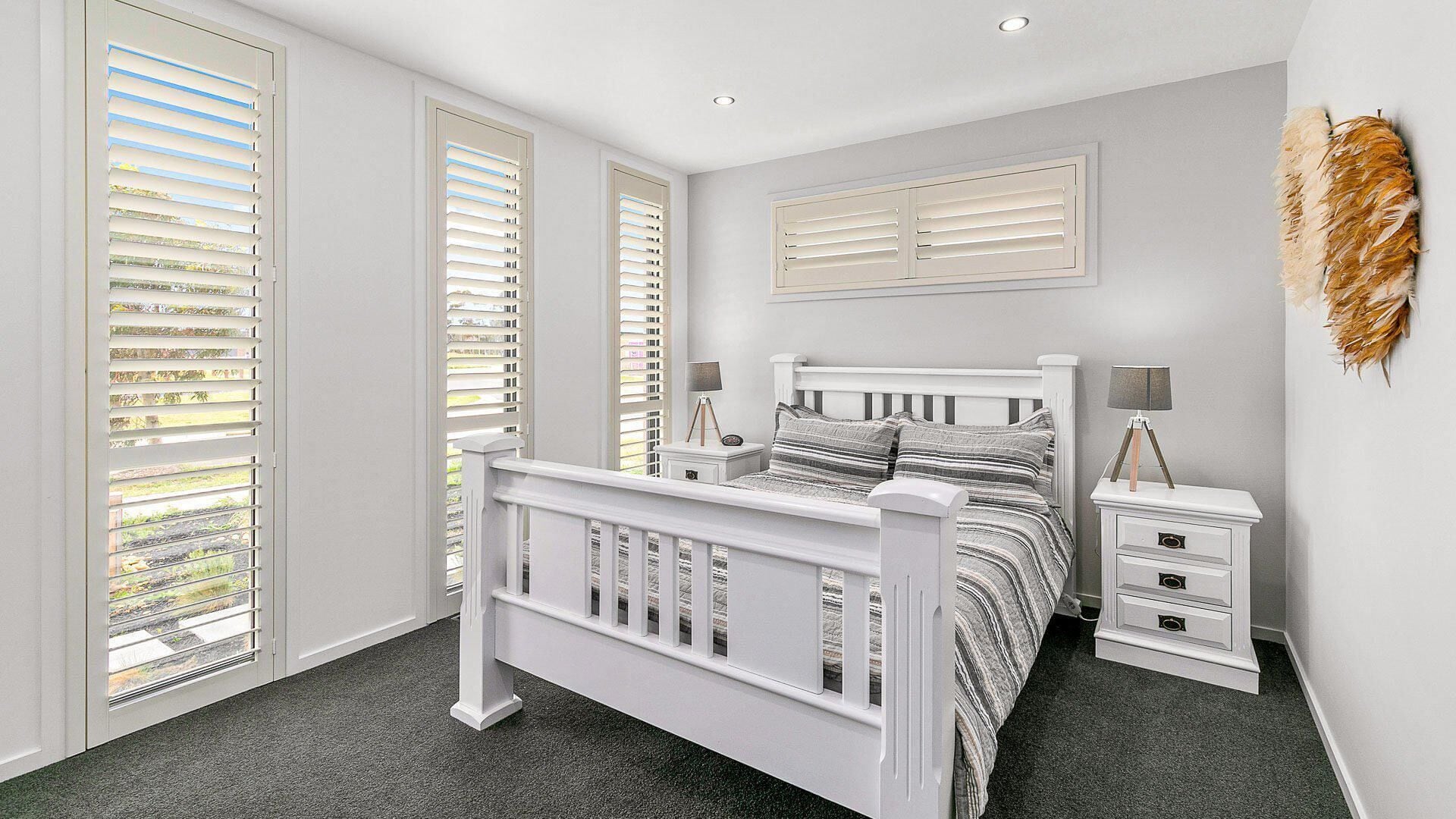 A bedroom with a white bed, two bedside tables, and a window with blinds.
