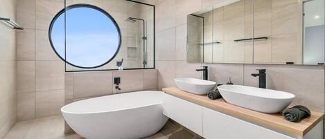 A modern bathroom with a freestanding bathtub, two sinks, and a large mirror.