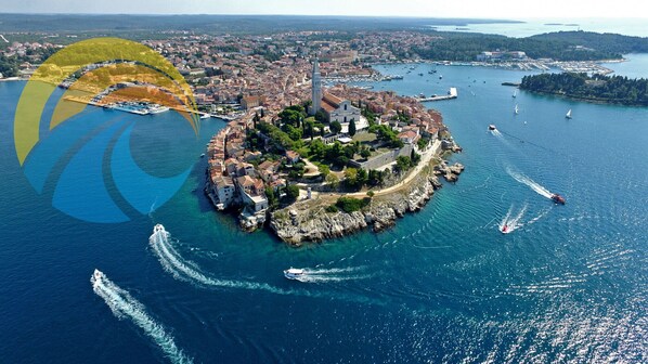 Vista aérea de un pueblo costero con una iglesia destacada, aguas azules cristalinas y barcos.