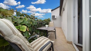 A balcony with a table and chairs, surrounded by greenery, and an air conditioning unit on the wall. - Apartment 1099/9467 (Istria - Rovinj), 400m from the beach (Rovinj)