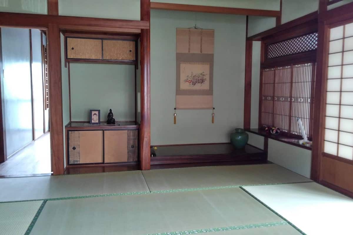 A traditional Japanese room with tatami flooring, a low wooden cabinet, a hanging scroll, and a shoji screen.