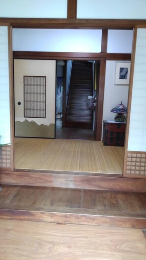 A traditional Japanese room with tatami flooring, a sliding door, a wooden staircase, and a small table with a lamp. - Guest House SAKICHI (Beppu)