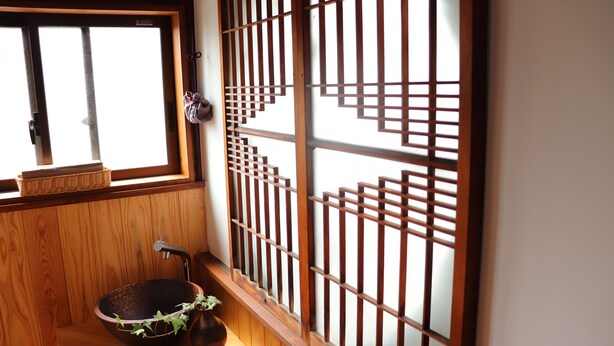 Ett traditionellt japanskt rum med träinredning, ett stort fönster med utsikt och en trävägg med ett rutmönster.