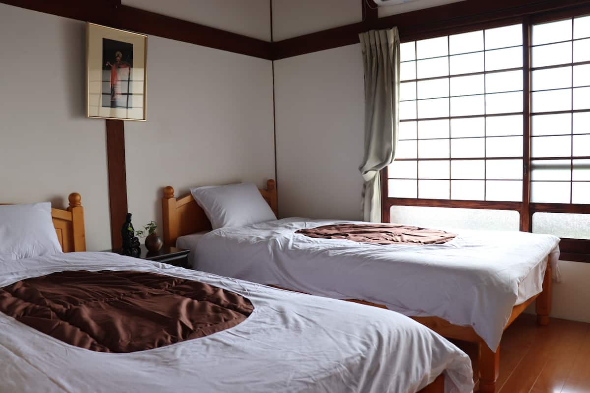 A room with two beds, wooden headboards, white bedding, a framed picture on the wall, and a window with curtains.
