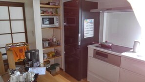 A compact kitchen with a microwave, refrigerator, and a small countertop. - Guest House SAKICHI (Beppu)