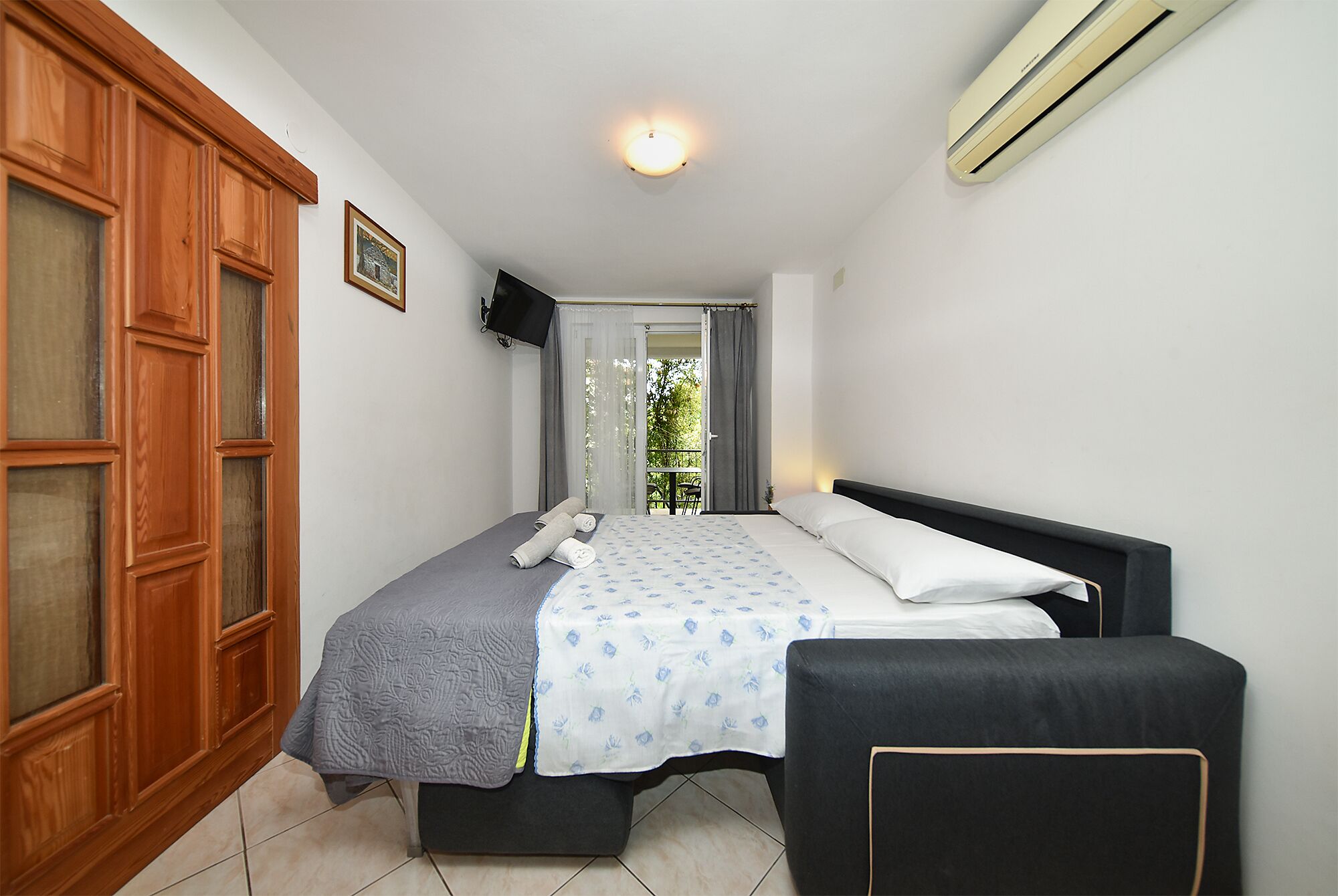 Quarto com cama, cadeira, guarda-roupa, televisão e ar condicionado.