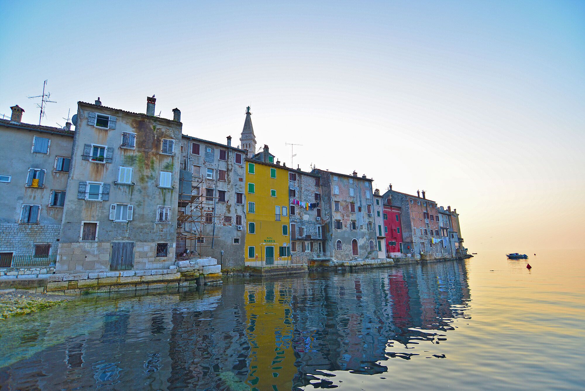 Un bâtiment situé au bord de l’eau, à plusieurs étages, dont certains sont partiellement recouverts d’échafaudages, et qui se reflète clairement dans l’eau.