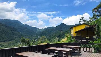 An outdoor dining area with wooden tables and chairs, overlooking a mountainous landscape.