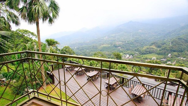 A wooden deck with outdoor furniture, surrounded by a metal railing, overlooking a lush green landscape with mountains in the distance. - Provence Villa (Nanzhuang)