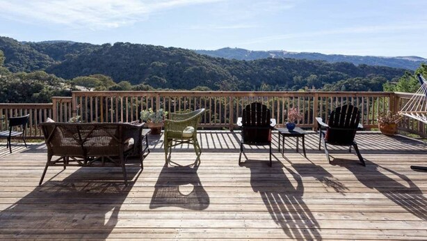 Een houten terras met wicker meubilair en een hangmat met uitzicht op een bebost glooiend landschap.