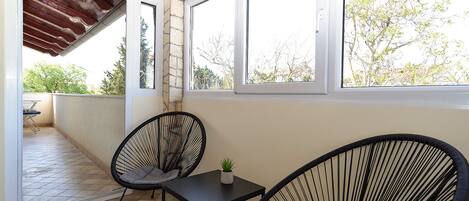 A balcony with two black wicker chairs, a small table, and a potted plant.