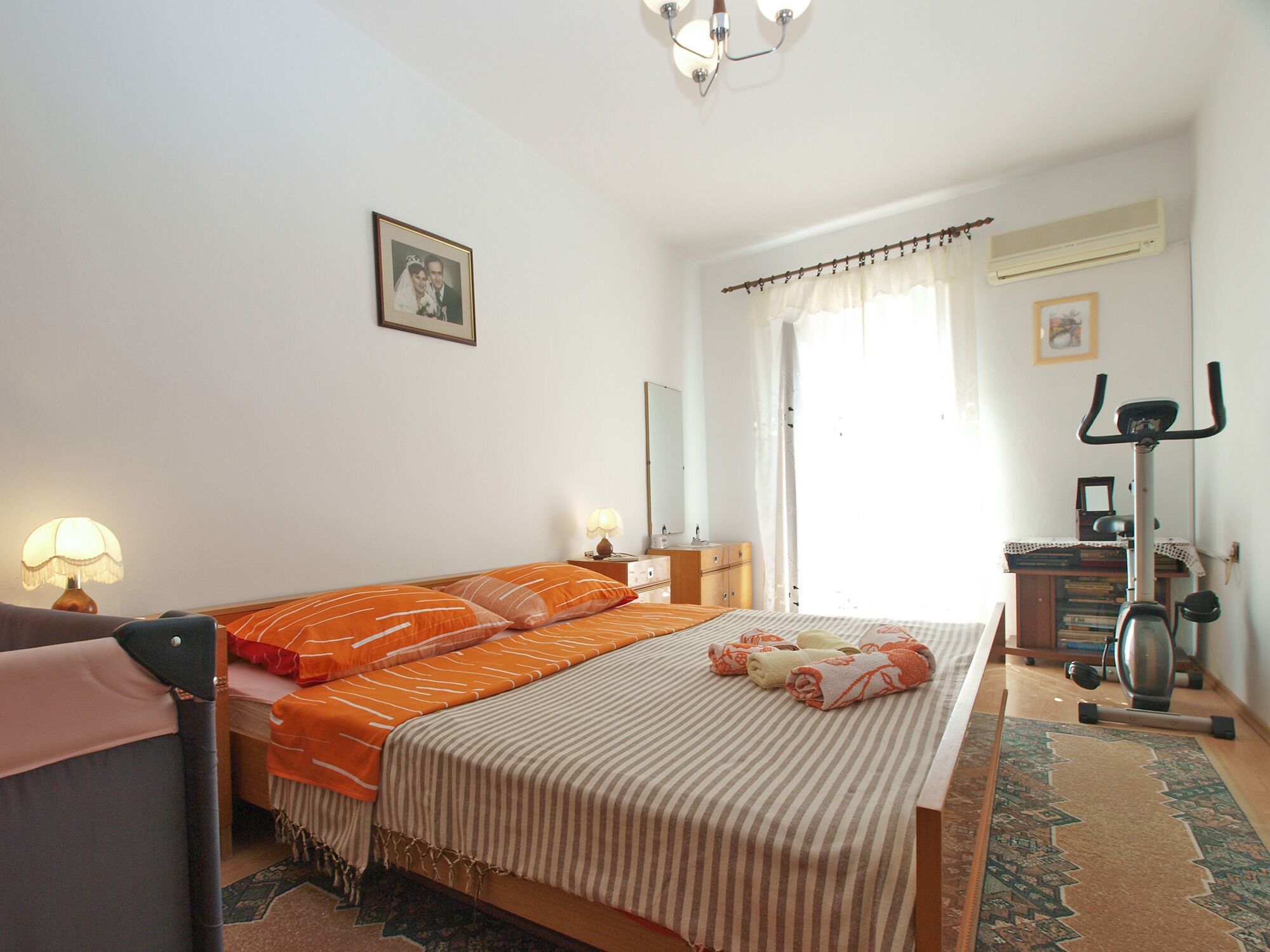 Une chambre à coucher comprenant un lit, deux tables de chevet, une lampe, un miroir, un appareil de climatisation et un vélo.
