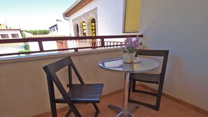 Ein Balkon mit zwei schwarzen Stühlen und einem kleinen runden Tisch, einer Topfpflanze sowie Blick auf Gebäude im Hintergrund.