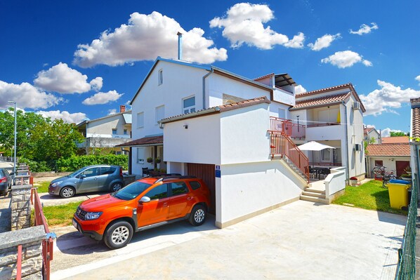 Um edifício residencial com garagem, uma escadaria que leva a uma varanda e um céu azul límpido.