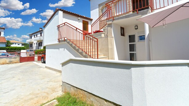 Ein zweistöckiges Haus mit roter Außenstufenverlauf, weißer Fassade und einem kleinen Balkon mit roter Brüstung.
