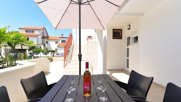 Une terrasse extérieure avec une table dressée pour deux personnes, une bouteille de vin et deux verres.