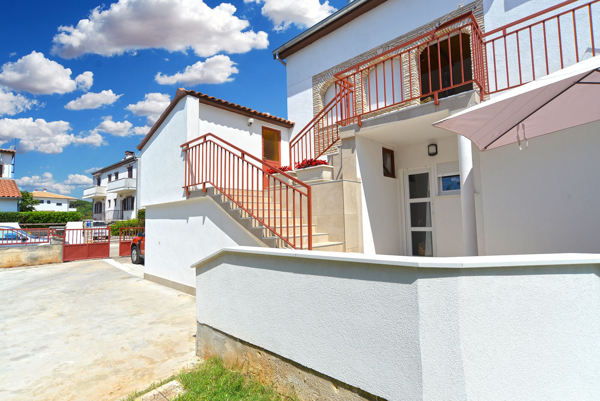 A two-story house with a red railing staircase, a white exterior, and a small balcony with a red railing.