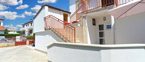 A two-story house with a red railing staircase, a white exterior, and a small balcony with a red railing.