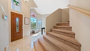 A spacious hallway with a wooden door, a staircase, and a bench. - LAS VEGAS LUXURY HOME, 5 BDRP, POOL W/HEATER, BBQ, GAMES (Las Vegas)