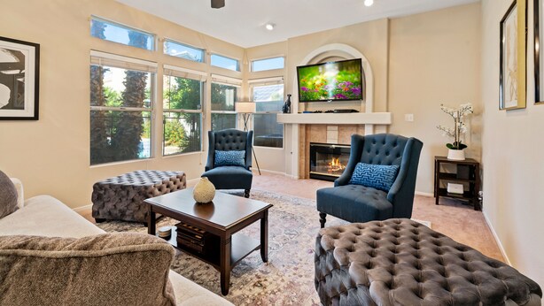 A spacious living room with a fireplace, large windows, and a ceiling fan. - LAS VEGAS LUXURY HOME, 5 BDRP, POOL W/HEATER, BBQ, GAMES (Las Vegas)