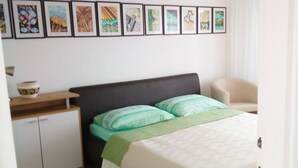 A bedroom with a bed, a chair, a desk, and a cabinet. There are framed pictures on the wall.