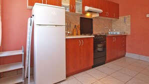 A compact kitchen with a white refrigerator, a stove, and wooden cabinets. - Apartment 1142/9868 (Istria - Valbandon), 750m from the beach (Valbandon)