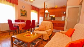 A living room with a sofa, a dining table with chairs, a kitchen area, and a clock on the wall. - Apartment 1142/9868 (Istria - Valbandon), 750m from the beach (Valbandon)