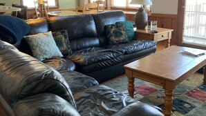 A cozy living room with a leather sofa, wooden coffee table, and a dining area with a lamp and chairs. - Crystal Mtn Condo, walk to lift,  soaking tub, short drive to Iron Fish & Lk MI (Thompsonville)