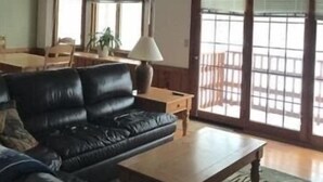 A spacious living room with a black leather sofa, a wooden coffee table, and a dining area with a table and chairs. - Crystal Mtn Condo, walk to lift,  soaking tub, short drive to Iron Fish & Lk MI (Thompsonville)