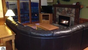 A cozy living room with a leather sofa, a wooden coffee table, a fireplace, and a television. - Crystal Mtn Condo, walk to lift,  soaking tub, short drive to Iron Fish & Lk MI (Thompsonville)