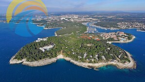 Ett flygbildsbild av en kuststad med en småbåtshamn, tät vegetation och bostadsområden.