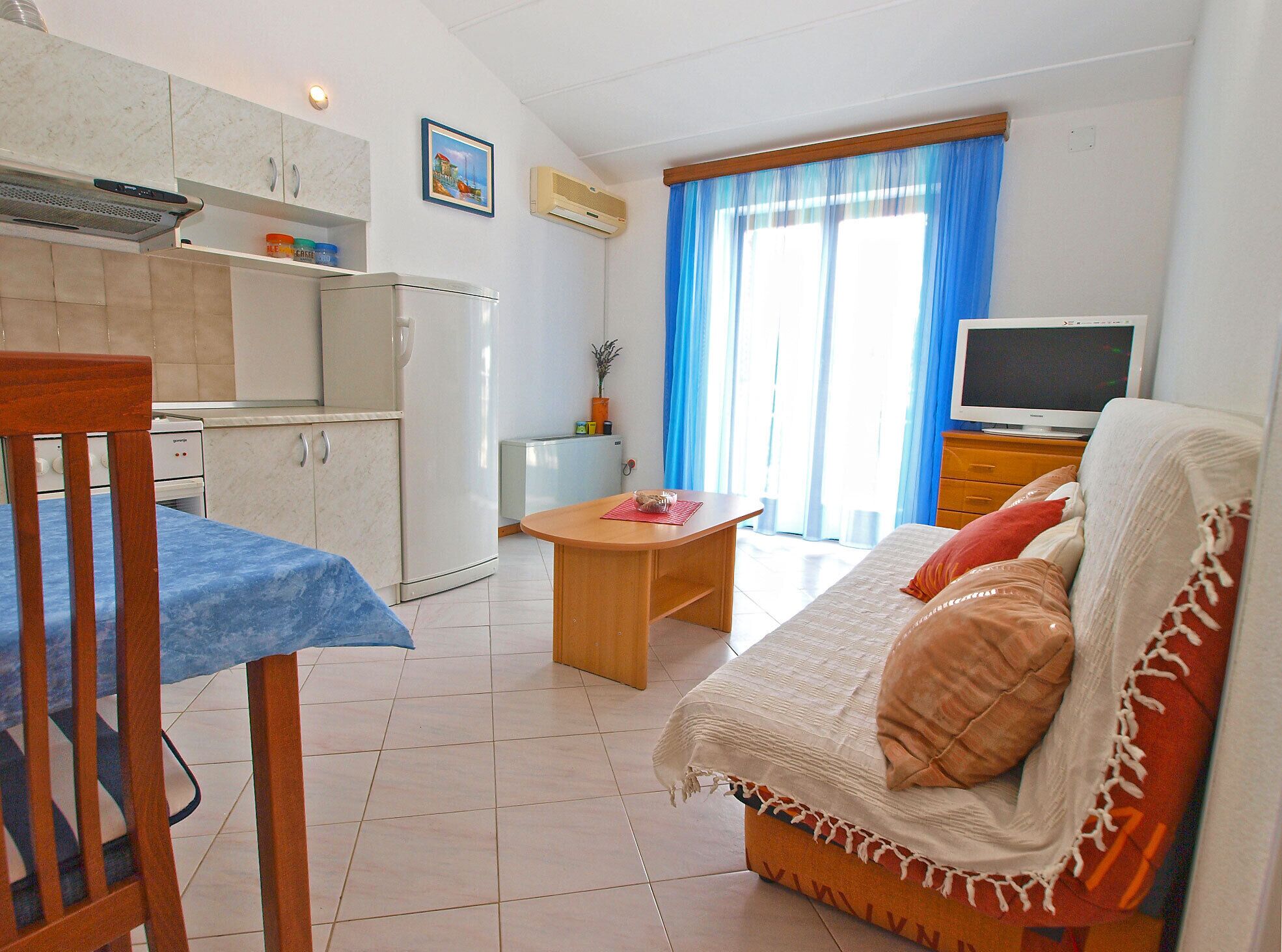 A compact living space with a kitchenette, a dining area, a sofa, and a TV.