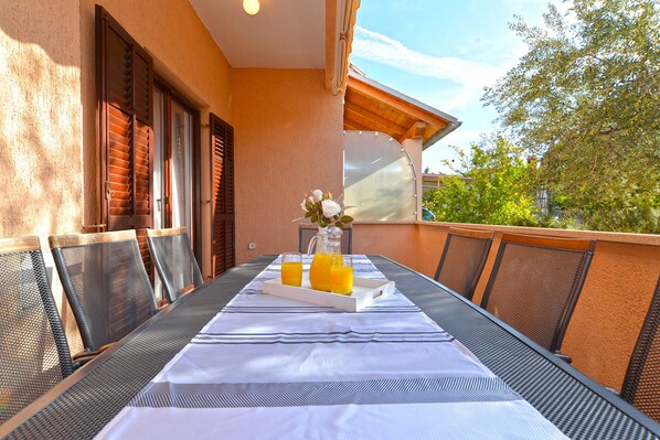 An outdoor dining area with a table set for two, featuring a white tablecloth and a pitcher of orange juice.