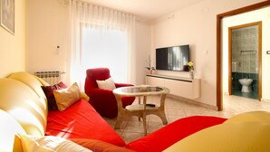A living room with a red sofa, a small round table, and a TV mounted on the wall. - Apartment 1179/10782 (Istria - Banjole), 500m from the beach (Banjole)