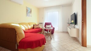 A living room with a sofa, a red armchair, a small table, and a television on the wall. - Apartment 1179/10782 (Istria - Banjole), 500m from the beach (Banjole)