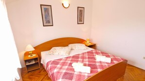 Ein ordentlich bezogenes Bett mit kariertem Überwurf und zwei Kissen, eine Nachttischlampe und ein gerahmtes Kunstwerk an der Wand.