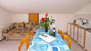 Ein kompakter Wohnbereich mit Sofa, Esstisch, Stühlen, einer Küchenzeile und einer Tür.