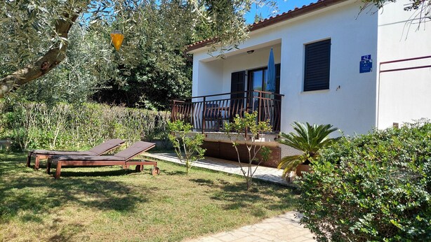 Un bâtiment à deux étages doté d’un balcon, d’un jardin avec une pelouse et de deux chaises longues.