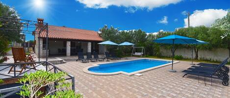 Un patio trasero con piscina, sillas de descanso y sombrillas.