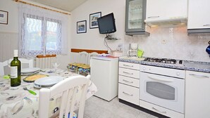 A compact kitchen with white cabinets, a built-in oven, a small refrigerator, a television mounted on the wall, and a dining area with a table set for two. - Apartment 1189/10858 (Istria - Premantura), 500m from the beach (Premantura)