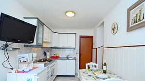 A compact kitchen with white cabinets, a built-in microwave, a gas stove, and a flat-screen TV mounted on the wall. - Apartment 1189/10858 (Istria - Premantura), 500m from the beach (Premantura)