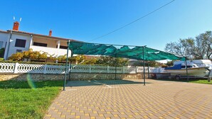 A paved outdoor area with a green canopy, a white fence, and a building with a red roof in the background. - Apartment 1189/10860 (Istria - Premantura), 500m from the beach (Premantura)