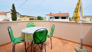 A terrace with a table and chairs, a yellow umbrella, and a view of houses in the background. - Apartment 1189/10860 (Istria - Premantura), 500m from the beach (Premantura)