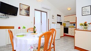 A dining area with a table set for two, a television mounted on the wall, and a kitchen in the background. - Apartment 1189/10860 (Istria - Premantura), 500m from the beach (Premantura)