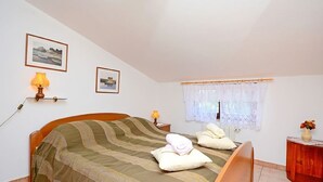 A bedroom with a bed, two bedside lamps, a window with lace curtains, and a small wooden side table with a vase. - Apartment 1189/10860 (Istria - Premantura), 500m from the beach (Premantura)