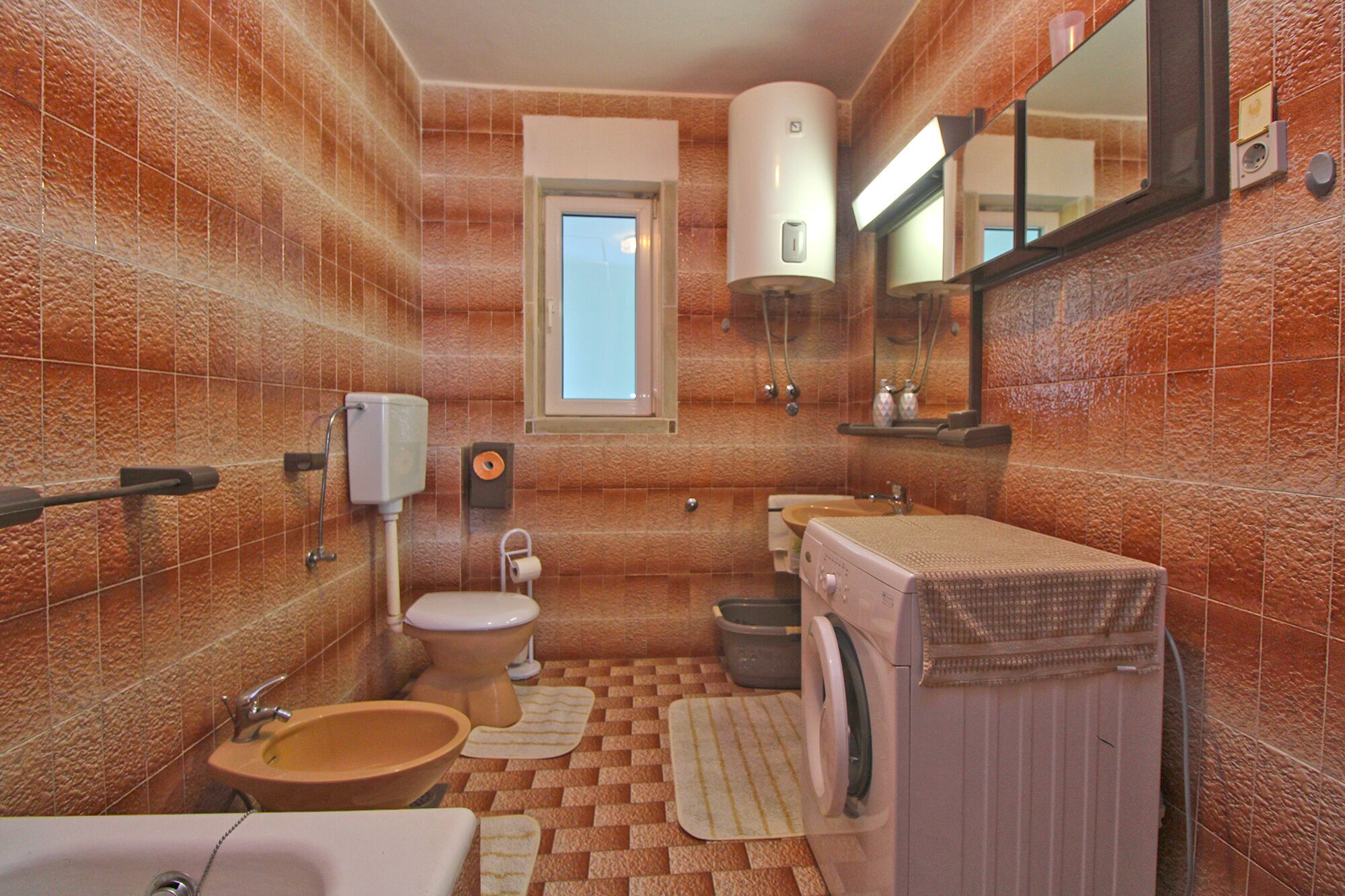 Un baño con inodoro, lavabo y lavadora, con piso de baldosas y ventana.