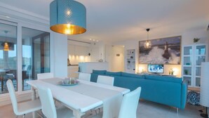 A modern living room with a white dining table, blue sofa, and a large painting on the wall. - Pura vida with balcony by Interhome (Bredene)