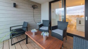 A balcony with a wooden floor, two wicker chairs, a small table with potted plants, and a glass door leading to an indoor area. - Pura vida with balcony by Interhome (Bredene)